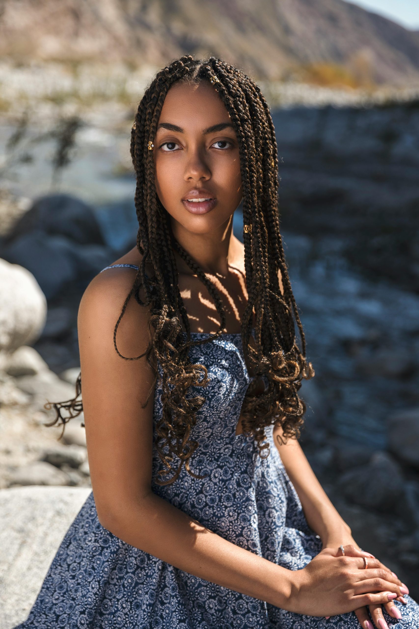 Portrait of a young woman with braided hair sitting outdoors in sunlight.